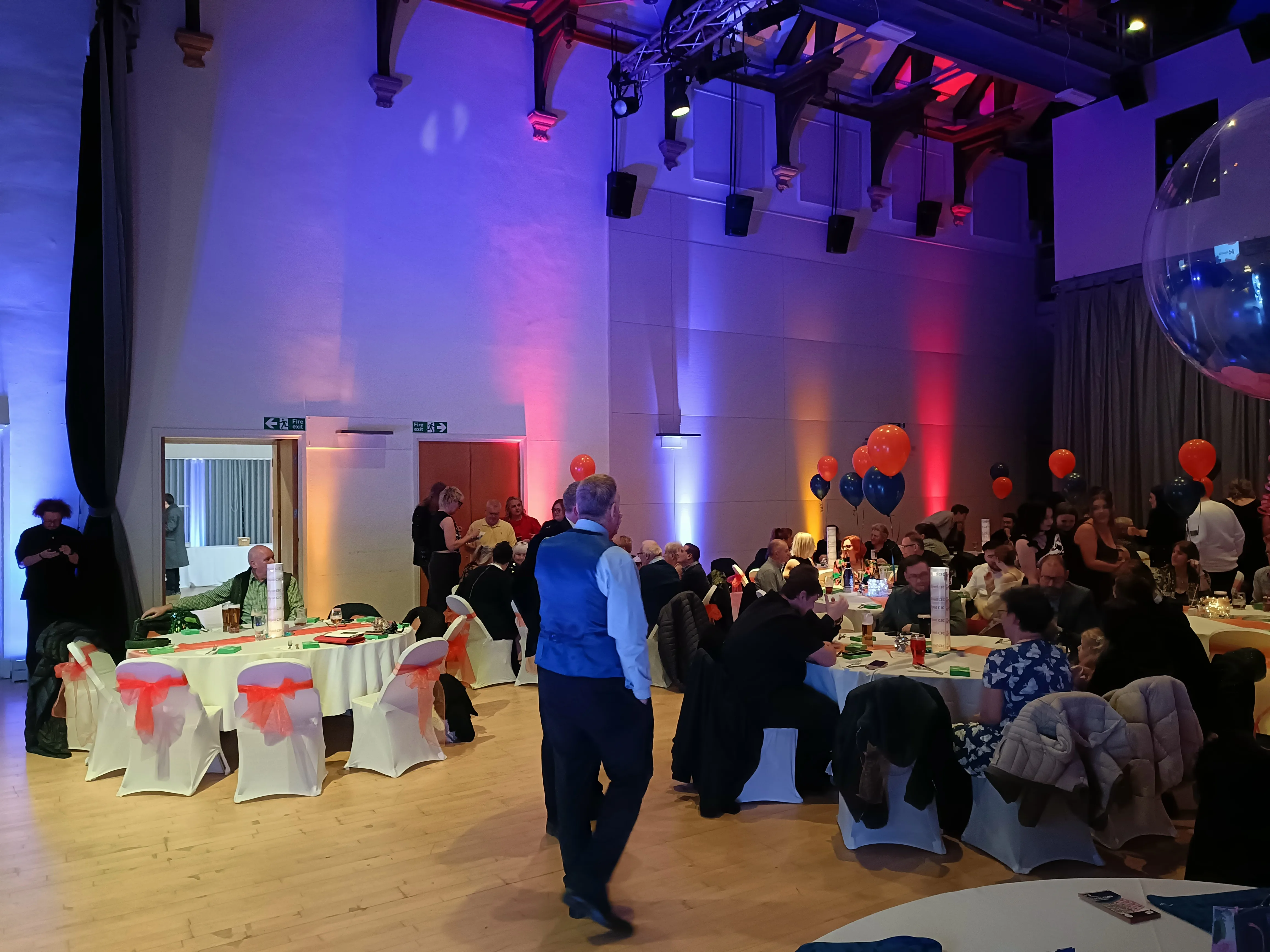 Full room view with guests seated at decorated tables under atmospheric uplighting